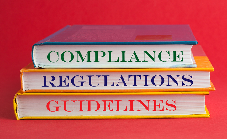 Books with words compliance, regulations and guidelines on red background.