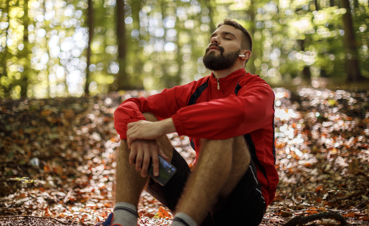 Portrait of relaxed young man with bluetooth headphones in forest