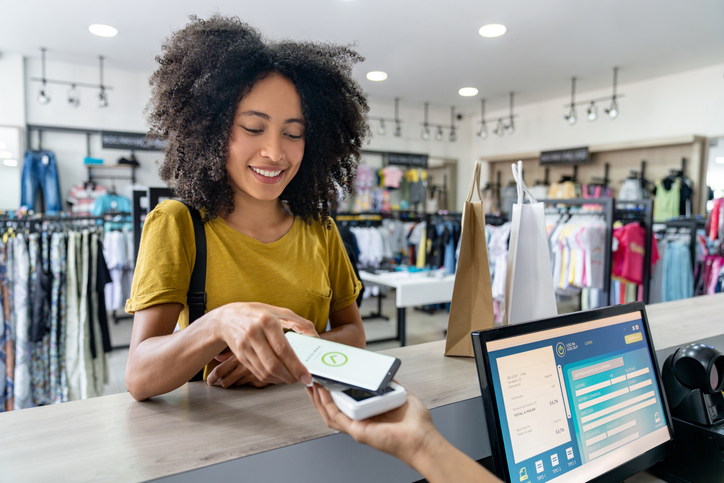 Happy Latin American woman making a mobile payment at a clothing store - contactless payment concepts