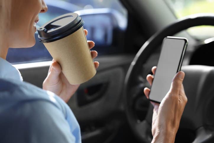 To-go drink. Woman with smartphone drinking coffee in car, closeup