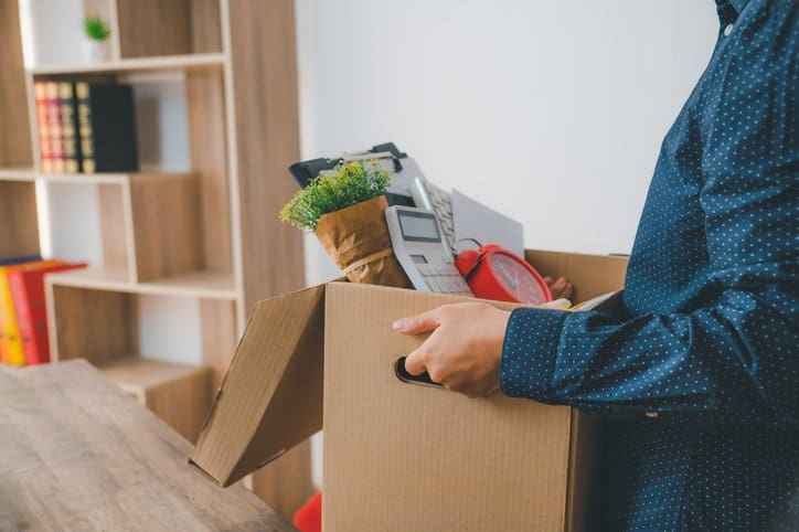 Female firm employee leaving the office with cardboard boxes containing office supplies and personal items after quitting to find a new job, being fired, or being fired from the company.
